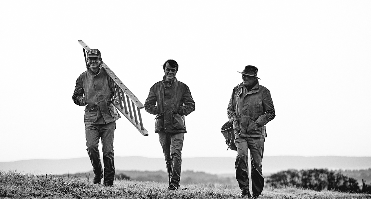 Three farmest walking across a field with ladders and baskets.